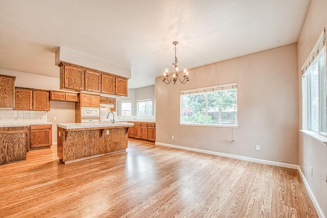 kitchen featuring white microwave, a notable chandelier, brown cabinets, and light wood-style floors