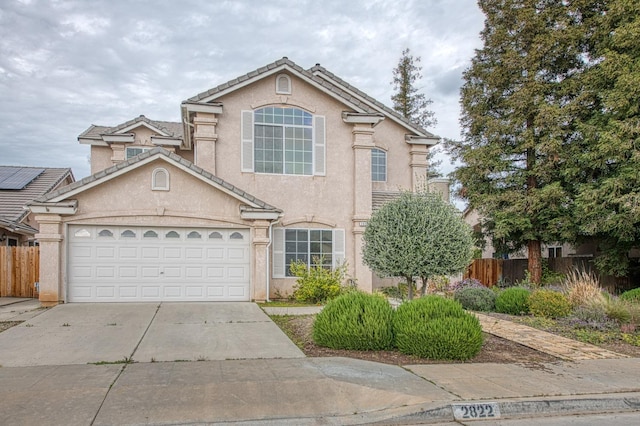 traditional-style home featuring fence, a garage, driveway, and stucco siding