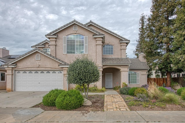 traditional home featuring fence, driveway, a chimney, stucco siding, and a tiled roof