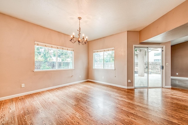 unfurnished room featuring a textured ceiling, baseboards, an inviting chandelier, and wood finished floors