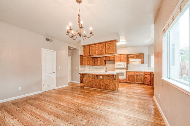 kitchen featuring light wood-style flooring, white appliances, an inviting chandelier, brown cabinetry, and decorative backsplash