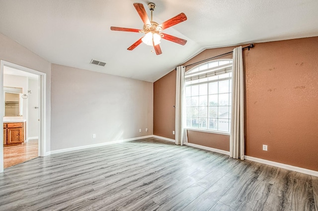 unfurnished room with visible vents, baseboards, lofted ceiling, wood finished floors, and a ceiling fan