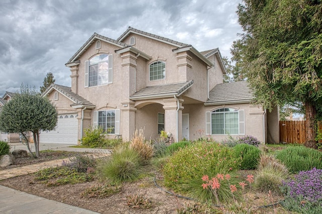 mediterranean / spanish home with stucco siding, a tile roof, concrete driveway, and fence