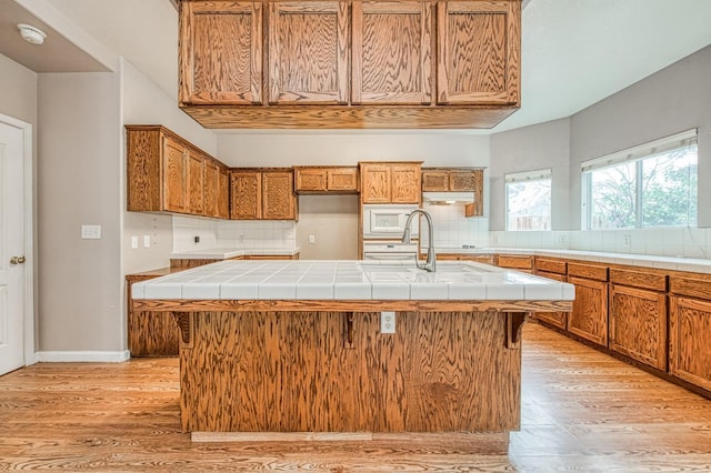 kitchen with a sink, decorative backsplash, white microwave, and light wood finished floors