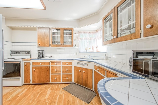 kitchen with tile countertops, light wood-style flooring, brown cabinets, electric range, and a sink