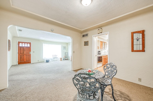 dining area featuring arched walkways, visible vents, light colored carpet, and a textured ceiling