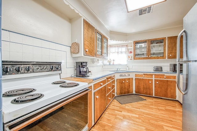 kitchen with light wood finished floors, brown cabinetry, ornamental molding, decorative backsplash, and white range with electric stovetop