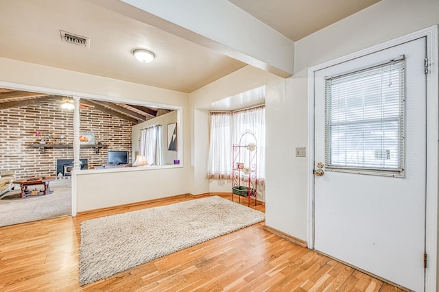 entrance foyer with visible vents, brick wall, wood finished floors, and vaulted ceiling with beams