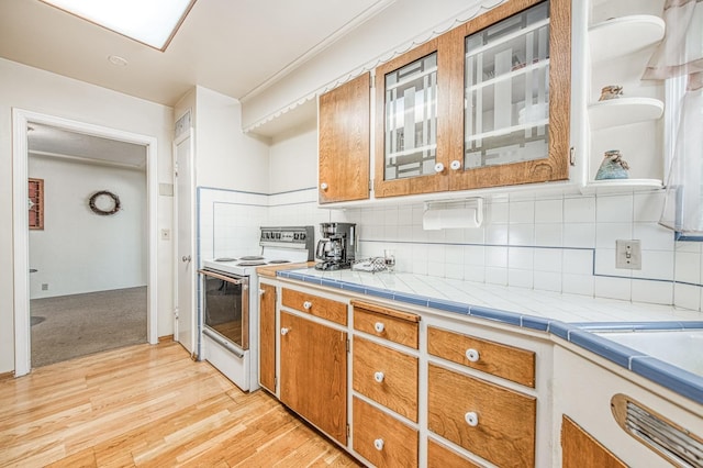 kitchen with light wood-type flooring, brown cabinets, electric stove, backsplash, and light countertops