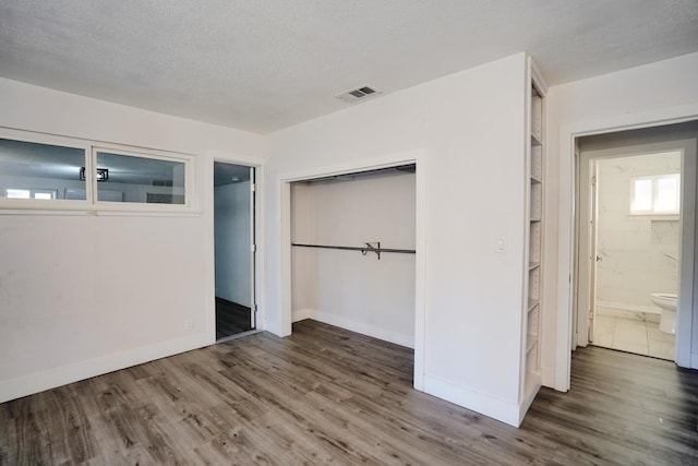 unfurnished bedroom featuring visible vents, a textured ceiling, wood finished floors, a closet, and baseboards