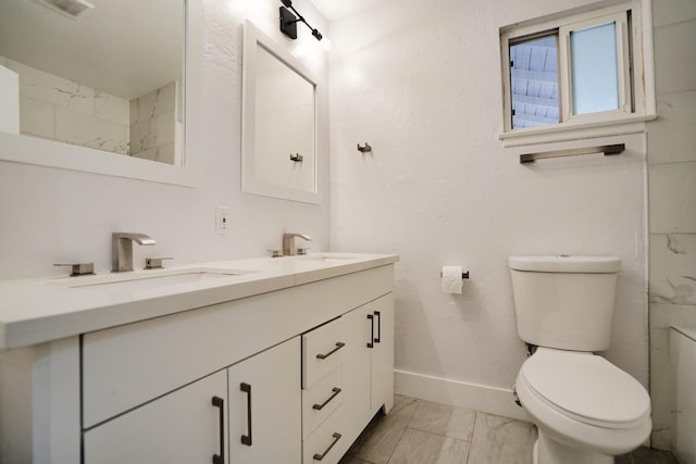 full bath with double vanity, toilet, marble finish floor, and a sink