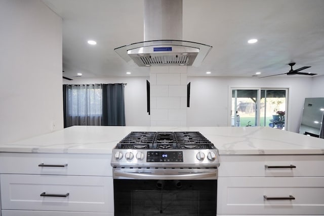 kitchen with stainless steel gas range oven, white cabinets, light stone counters, and island range hood