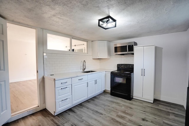 kitchen with light wood finished floors, a sink, light countertops, black range with electric stovetop, and stainless steel microwave