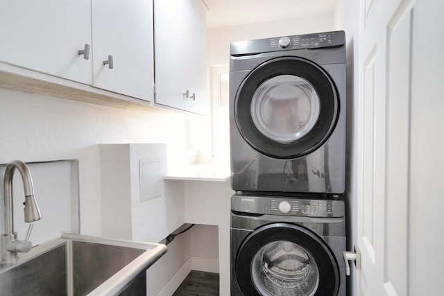 washroom with a sink, cabinet space, stacked washer / dryer, baseboards, and dark wood-style flooring