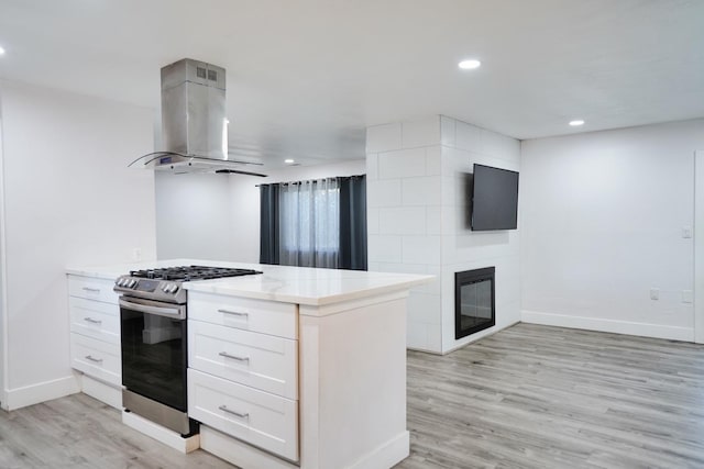 kitchen with island exhaust hood, light stone counters, stainless steel range with gas cooktop, white cabinets, and light wood finished floors