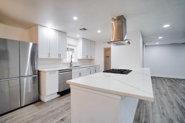 kitchen featuring light wood-type flooring, white cabinets, stainless steel appliances, wall chimney exhaust hood, and a sink