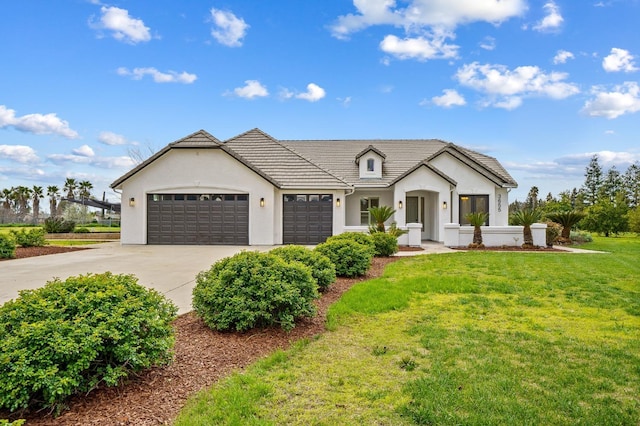 modern farmhouse featuring driveway, an attached garage, stucco siding, a front lawn, and a tiled roof