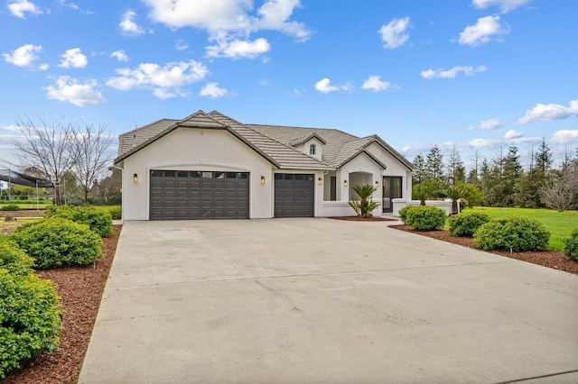 view of front of house with stucco siding, driveway, an attached garage, and a tiled roof