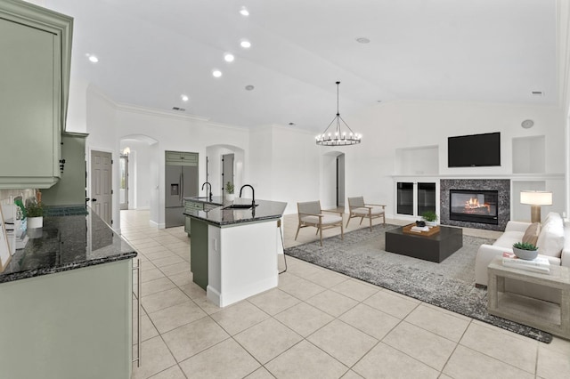 kitchen with a sink, arched walkways, green cabinetry, lofted ceiling, and light tile patterned floors