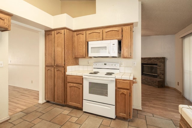 kitchen featuring white appliances, tile countertops, a brick fireplace, and light wood-style floors