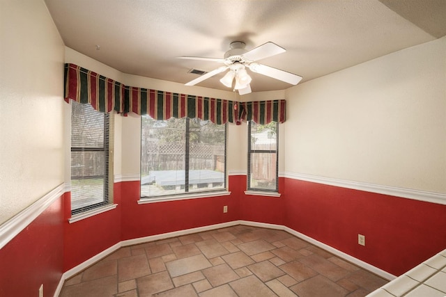 empty room featuring stone finish flooring, a ceiling fan, visible vents, and baseboards