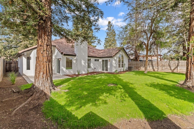 back of house with stucco siding, a yard, a fenced backyard, and a tile roof