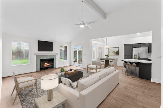 living room featuring light wood-type flooring, beam ceiling, a healthy amount of sunlight, and a tile fireplace