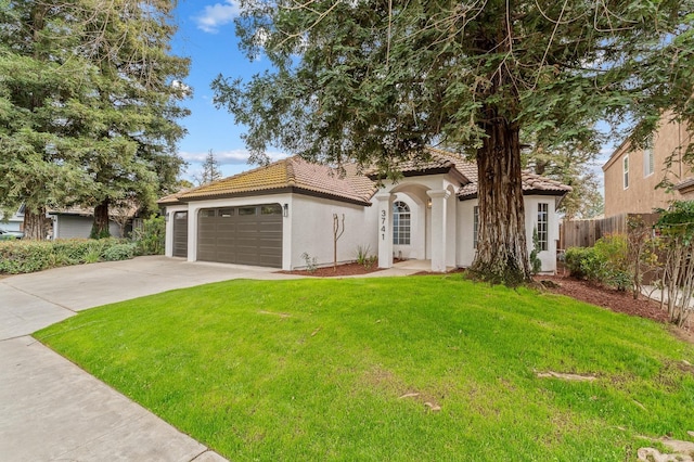 mediterranean / spanish home featuring stucco siding, a front lawn, a tile roof, fence, and concrete driveway