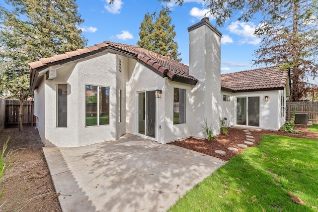 rear view of property featuring stucco siding, a tile roof, a patio, fence, and a chimney