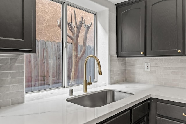 kitchen with a sink, light stone counters, and backsplash