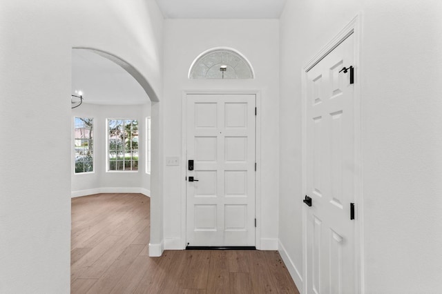 entryway with arched walkways, baseboards, and wood finished floors