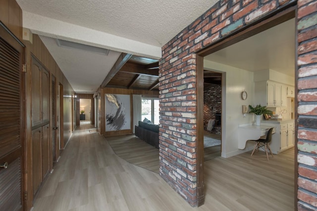 corridor with beam ceiling, baseboards, a textured ceiling, and light wood-style floors