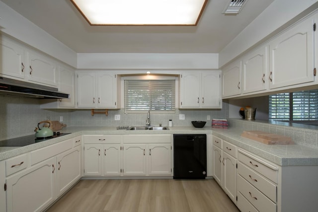 kitchen with black appliances, light wood-style flooring, a sink, under cabinet range hood, and white cabinetry