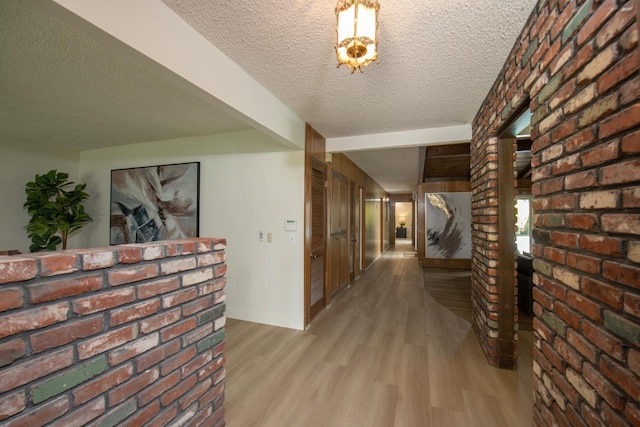 hall with beam ceiling, wood finished floors, brick wall, and a textured ceiling