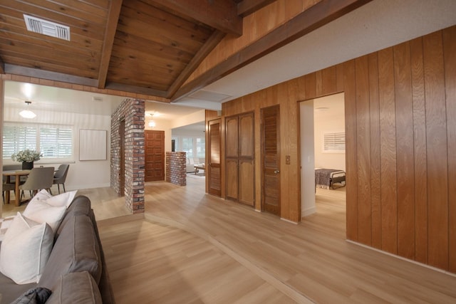 living room with visible vents, light wood-style flooring, vaulted ceiling with beams, decorative columns, and wood walls