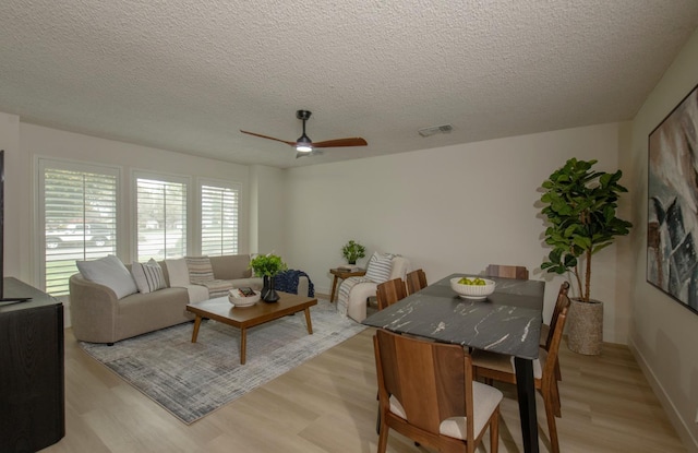 living area featuring ceiling fan, visible vents, a textured ceiling, and light wood-style flooring