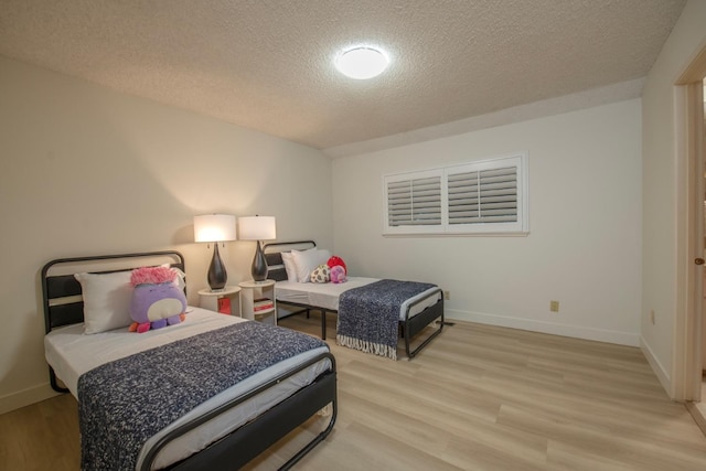 bedroom featuring a textured ceiling, baseboards, and light wood-style floors