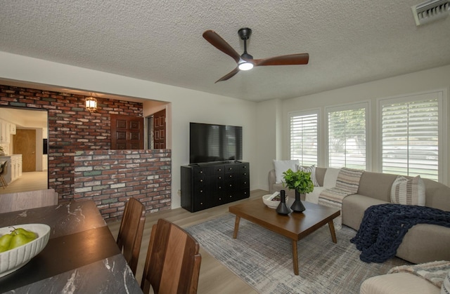 living room with a textured ceiling, wood finished floors, visible vents, and ceiling fan