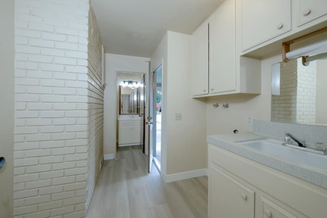 clothes washing area with light wood-style flooring, baseboards, brick wall, and a sink