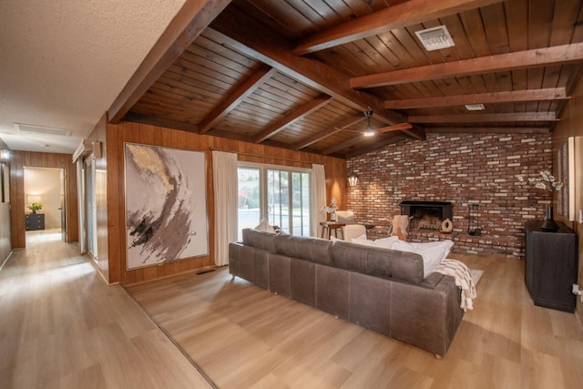 living area featuring visible vents, light wood-style flooring, wood walls, a fireplace, and ceiling fan