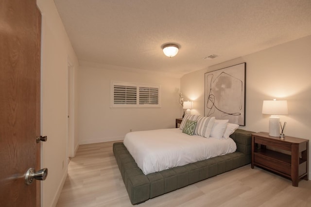 bedroom with visible vents, light wood-style flooring, a textured ceiling, and baseboards