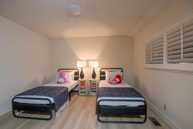 bedroom with visible vents, a textured ceiling, lofted ceiling, and wood finished floors