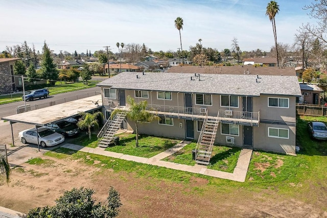 view of front facade with a front yard, a shingled roof, stairs, stucco siding, and a residential view