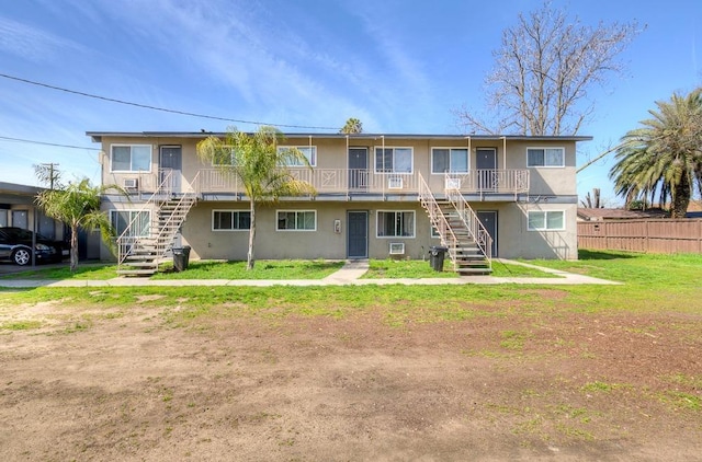 rear view of property featuring stucco siding, a yard, stairs, and fence