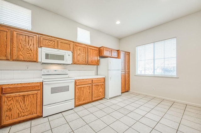 kitchen featuring tile countertops, white appliances, light tile patterned flooring, brown cabinetry, and baseboards