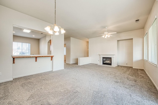 unfurnished living room with arched walkways, a glass covered fireplace, a healthy amount of sunlight, and carpet