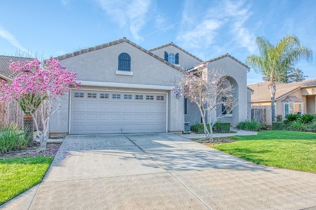 mediterranean / spanish house with a tiled roof, concrete driveway, a front yard, stucco siding, and a garage