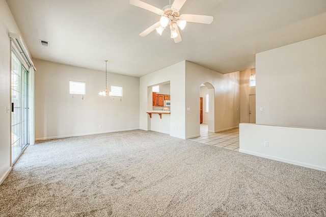 unfurnished living room featuring visible vents, baseboards, ceiling fan, light carpet, and arched walkways