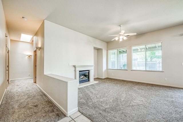 unfurnished living room with baseboards, a glass covered fireplace, a ceiling fan, and carpet