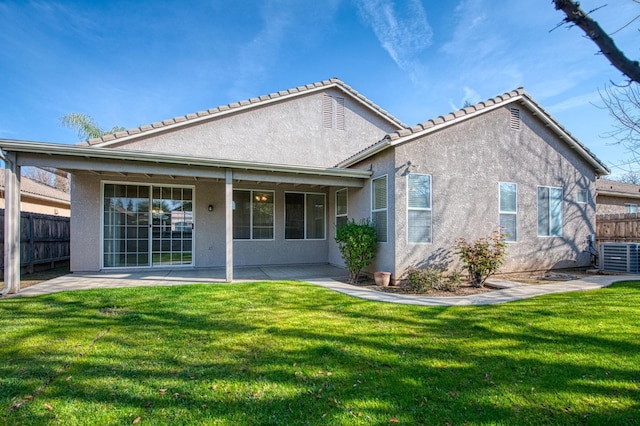 rear view of house featuring stucco siding, a lawn, and fence